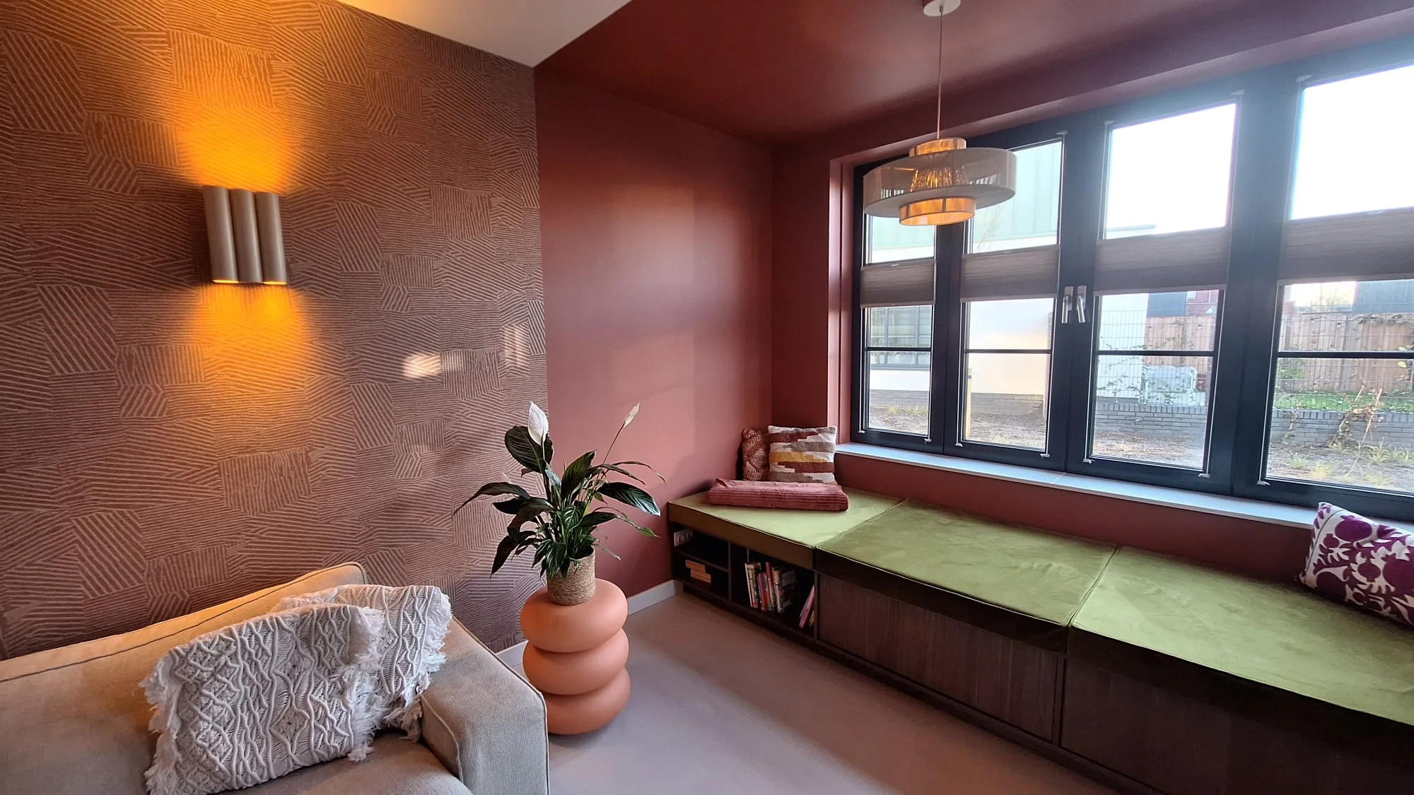 Geschilderde muren en plafond in een warme terracottatint met behangen accentwand in een woning in Naarden